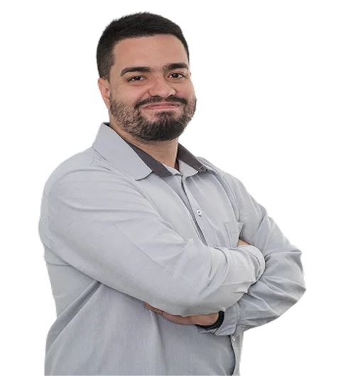 Retrato profesional de un consultor integrante del equipo de Insega, con barba, sonriendo y vistiendo el uniforme gris corporativo, posando con los brazos cruzados sobre fondo blanco.